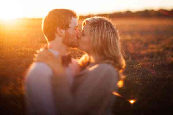 An engaged couple kissing in front of a sunset