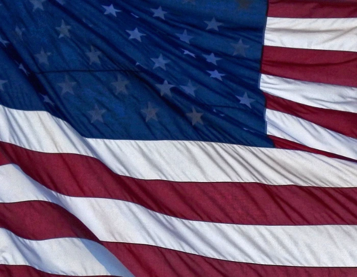 A crop of an American flag, blowing in the wind, with sunlight shining through the fabric