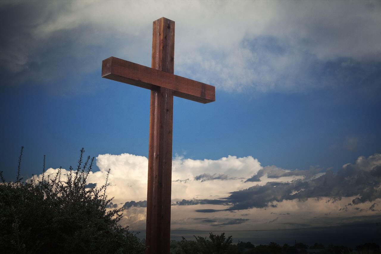 A wooden cross statue stands tall against a backdrop of post-storm clouds in a field during early morning